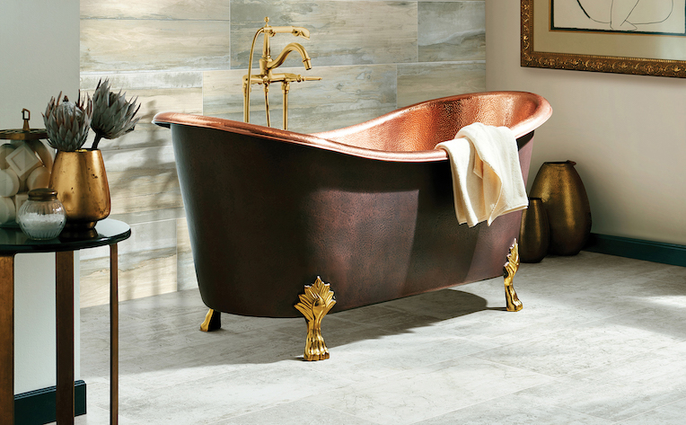 grey tile flooring in a bright bathroom with wood look tile accent wall and a stand alone copper tub